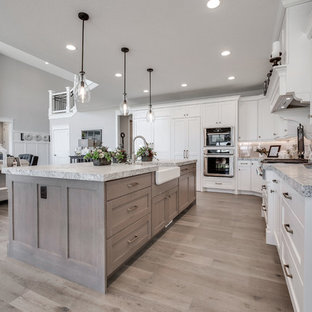 Mid-sized craftsman open concept kitchen ideas - Inspiration for a mid-sized craftsman l-shaped medium tone wood floor and brown floor open concept kitchen remodel in Salt Lake City with a farmhouse sink, shaker cabinets, white cabinets, marble countertops, white backsplash, subway tile backsplash, paneled appliances and an island