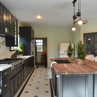 This is an example of a large eclectic single-wall open plan kitchen in Houston with an undermount sink, glass-front cabinets, black cabinets, wood benchtops, white splashback, ceramic splashback, stainless steel appliances, ceramic floors and with island.