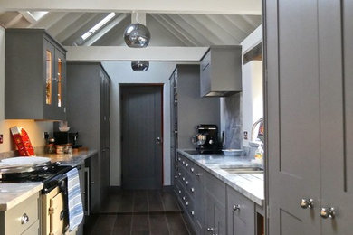 Photo of a contemporary galley kitchen/diner in Oxfordshire with a built-in sink, shaker cabinets, grey cabinets, marble worktops, grey splashback, black appliances and porcelain flooring.