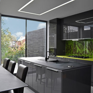Photo of a contemporary galley kitchen/diner in London with a built-in sink, flat-panel cabinets, black cabinets, green splashback and black appliances.