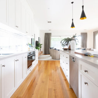 Design ideas for a large transitional galley kitchen in Melbourne with an undermount sink, shaker cabinets, white cabinets, window splashback, stainless steel appliances, multiple islands, brown floor and grey benchtop.