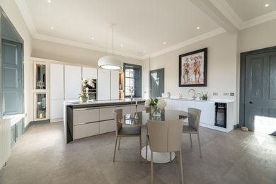 This is an example of a large shabby-chic style l-shaped open plan kitchen in Edinburgh with an integrated sink, flat-panel cabinets, yellow cabinets, quartz worktops, beige splashback, stone tiled splashback, stainless steel appliances, cement flooring, an island, beige floors and white worktops.