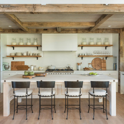 Country u-shaped medium tone wood floor and brown floor kitchen photo in Boston with a farmhouse sink, shaker cabinets, white cabinets, white backsplash, stone slab backsplash, paneled appliances, an island and white countertops