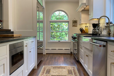 Example of a small galley medium tone wood floor and brown floor eat-in kitchen design in New York with a farmhouse sink, beaded inset cabinets, white cabinets, granite countertops, white backsplash, subway tile backsplash, stainless steel appliances, no island and gray countertops