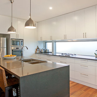 Photo of a contemporary u-shaped kitchen in Central Coast with an undermount sink, flat-panel cabinets, white cabinets, window splashback, stainless steel appliances, medium hardwood floors, with island, brown floor and grey benchtop.