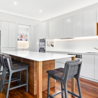 Large contemporary l-shaped kitchen in Sydney with an undermount sink, flat-panel cabinets, white cabinets, white splashback, with island, brown floor and white benchtop.