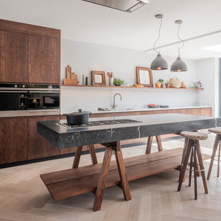 This is an example of a large contemporary single-wall open plan kitchen in London with an integrated sink, flat-panel cabinets, dark wood cabinets, marble benchtops, stainless steel appliances, medium hardwood floors, with island and white benchtop.