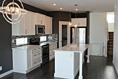 Example of a mid-sized minimalist l-shaped dark wood floor eat-in kitchen design in Calgary with a double-bowl sink, recessed-panel cabinets, white cabinets, granite countertops, gray backsplash, mosaic tile backsplash, stainless steel appliances and an island