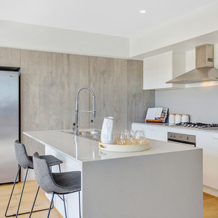 Inspiration for a contemporary l-shaped kitchen in Brisbane with a drop-in sink, flat-panel cabinets, white cabinets, grey splashback, stainless steel appliances, light hardwood floors, with island, beige floor and white benchtop.