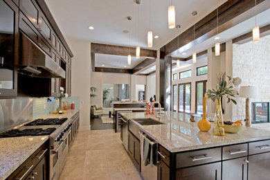 Large trendy l-shaped travertine floor open concept kitchen photo in Los Angeles with a farmhouse sink, shaker cabinets, dark wood cabinets, quartzite countertops, blue backsplash, glass tile backsplash, stainless steel appliances and an island