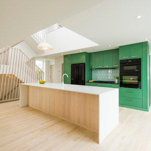Scandinavian galley open plan kitchen in DC Metro with flat-panel cabinets, green cabinets, green splashback, black appliances, light hardwood floors and with island.