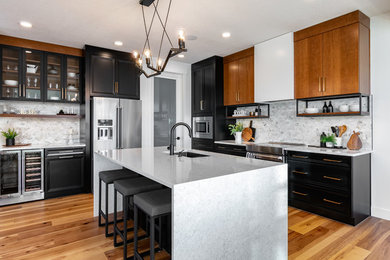 Foto på ett mellanstort vintage vit l-kök, med en undermonterad diskho, luckor med infälld panel, svarta skåp, bänkskiva i kvartsit, vitt stänkskydd, rostfria vitvaror, mellanmörkt trägolv, en köksö och brunt golv