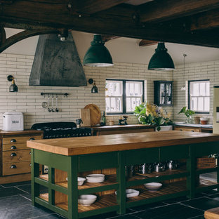 Country l-shaped kitchen in London with a farmhouse sink, open cabinets, green cabinets, wood benchtops, white splashback, subway tile splashback, with island and grey floor.