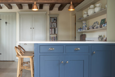Ejemplo de cocina campestre con armarios estilo shaker, puertas de armario azules, suelo beige y encimeras blancas
