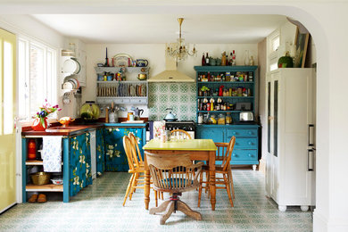 На фото: угловая кухня в стиле фьюжн с обеденным столом, синими фасадами и зеленым фартуком
