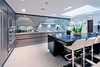 This is an example of a medium sized contemporary l-shaped enclosed kitchen in London with a built-in sink, flat-panel cabinets, grey cabinets, composite countertops, white splashback, glass sheet splashback, stainless steel appliances, limestone flooring and an island.