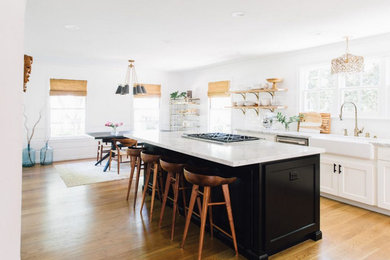 Foto de cocina comedor lineal clásica renovada de tamaño medio con fregadero sobremueble, armarios estilo shaker, puertas de armario blancas, encimera de cuarcita, salpicadero blanco, electrodomésticos de acero inoxidable, suelo de madera clara y una isla