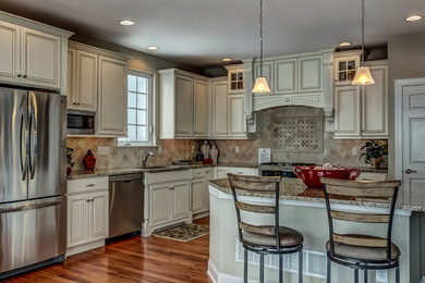 Example of a large classic l-shaped medium tone wood floor eat-in kitchen design in Philadelphia with an undermount sink, raised-panel cabinets, white cabinets, granite countertops, beige backsplash, limestone backsplash, stainless steel appliances and an island