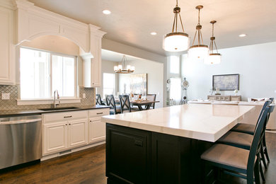 Example of a large arts and crafts l-shaped medium tone wood floor eat-in kitchen design in Salt Lake City with an undermount sink, recessed-panel cabinets, white cabinets, quartz countertops, metallic backsplash, ceramic backsplash, stainless steel appliances and an island