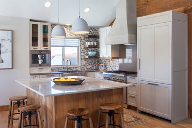 Photo of a rustic l-shaped kitchen in Denver with a belfast sink, shaker cabinets, grey cabinets, multi-coloured splashback, mosaic tiled splashback, stainless steel appliances, medium hardwood flooring, an island, brown floors and grey worktops.