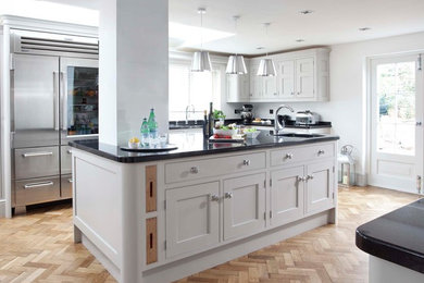 This is an example of a medium sized classic single-wall kitchen in Other with shaker cabinets, grey cabinets, granite worktops, grey splashback, metro tiled splashback, light hardwood flooring, an island and brown floors.