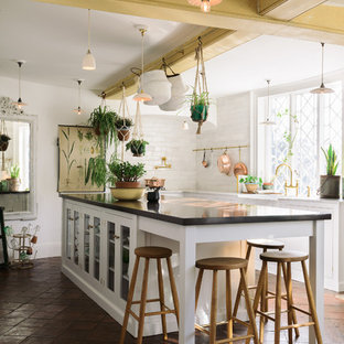 Design ideas for a large country kitchen in Other with a farmhouse sink, white cabinets, marble benchtops, white splashback, subway tile splashback, terra-cotta floors, with island, brown floor, glass-front cabinets and black benchtop.