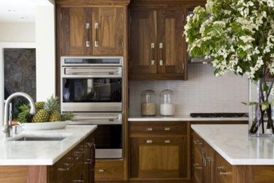 Imagen de cocinas en L contemporánea grande con armarios estilo shaker, puertas de armario de madera oscura, salpicadero blanco, electrodomésticos de acero inoxidable y dos o más islas