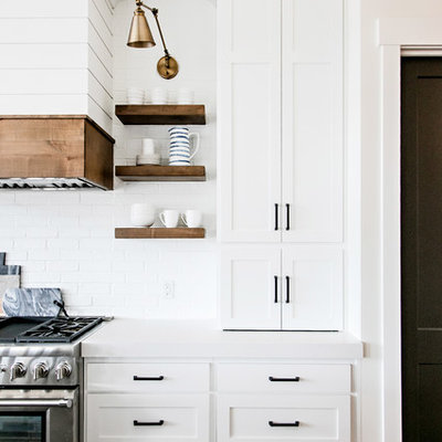 Mid-sized farmhouse medium tone wood floor and brown floor kitchen photo in Salt Lake City with a farmhouse sink, shaker cabinets, white cabinets, quartz countertops, white backsplash, subway tile backsplash, stainless steel appliances, an island and white countertops
