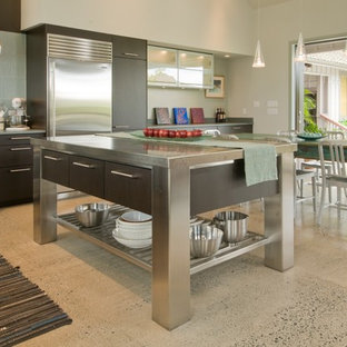 Ejemplo de cocina comedor tropical con armarios con paneles lisos, electrodomésticos de acero inoxidable, encimera de acero inoxidable y puertas de armario de madera en tonos medios