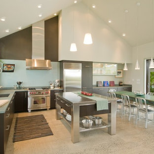 Diseño de cocina en L, exótica, abierta, con armarios con paneles lisos, electrodomésticos de acero inoxidable, encimera de acero inoxidable, puertas de armario de madera en tonos medios, salpicadero azul y encimeras verdes