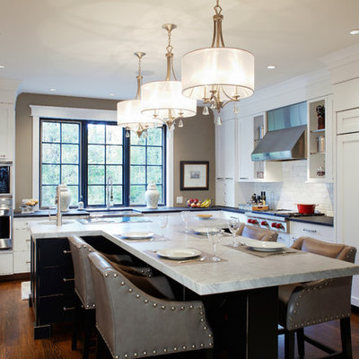 Example of a large classic l-shaped dark wood floor enclosed kitchen design in Philadelphia with a farmhouse sink, marble countertops, paneled appliances, shaker cabinets, white cabinets, white backsplash, subway tile backsplash and an island