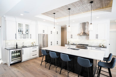 Farmhouse medium tone wood floor eat-in kitchen photo in Grand Rapids with an undermount sink, shaker cabinets, white cabinets, quartz countertops, gray backsplash, marble backsplash, stainless steel appliances, an island and white countertops