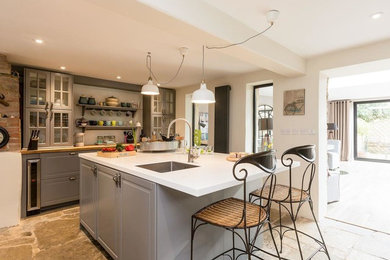 This is an example of a large rural l-shaped kitchen/diner in Oxfordshire with shaker cabinets, grey cabinets, composite countertops, limestone flooring, an island, grey floors and a submerged sink.