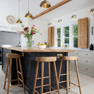 Medium sized country l-shaped kitchen in Hertfordshire with a submerged sink, recessed-panel cabinets, grey cabinets, wood worktops, white splashback, stainless steel appliances, an island, grey floors and beige worktops.