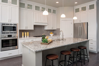 Inspiration for a large transitional l-shaped dark wood floor open concept kitchen remodel in Boise with an undermount sink, raised-panel cabinets, white cabinets, granite countertops, gray backsplash, stainless steel appliances, an island and ceramic backsplash