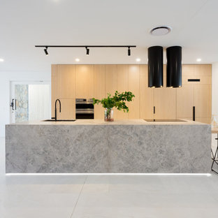 Ispirazione per una grande cucina contemporanea con lavello sottopiano, ante in legno chiaro, top in pietra calcarea, elettrodomestici neri, pavimento in marmo, pavimento bianco, top grigio e ante lisce