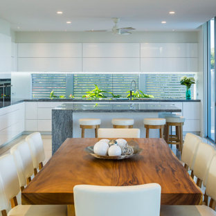 This is an example of a contemporary l-shaped eat-in kitchen in Cairns with an undermount sink, granite benchtops, white splashback, glass sheet splashback, stainless steel appliances, porcelain floors, with island, white floor, grey benchtop, flat-panel cabinets and white cabinets.