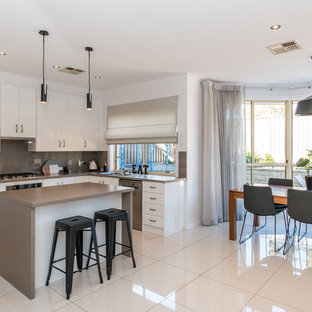 Scandinavian l-shaped eat-in kitchen in Adelaide with a drop-in sink, flat-panel cabinets, white cabinets, beige splashback, glass sheet splashback, stainless steel appliances, with island, white floor and beige benchtop.