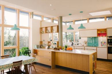 Large midcentury u-shaped open plan kitchen in Manchester with flat-panel cabinets, white cabinets, composite countertops, blue splashback, glass sheet splashback, stainless steel appliances, no island and white worktops.