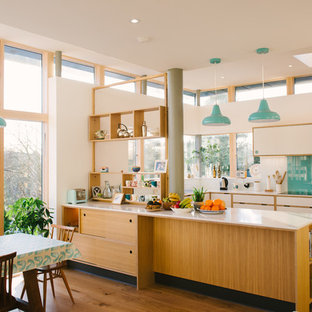 Large midcentury u-shaped open plan kitchen in Manchester with flat-panel cabinets, white cabinets, composite countertops, blue splashback, glass sheet splashback, stainless steel appliances, no island and white worktops.