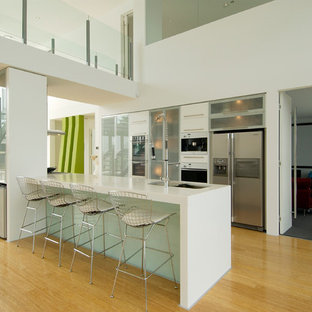 Photo of a contemporary galley kitchen in Gold Coast - Tweed with an undermount sink, glass-front cabinets, stainless steel appliances, medium hardwood floors, with island, brown floor and white benchtop.