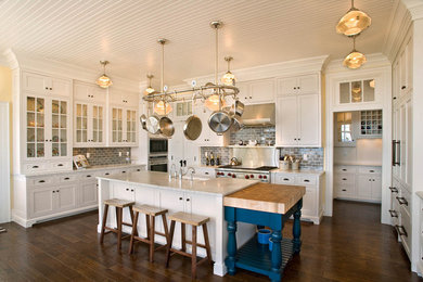 Inspiration for a large timeless u-shaped medium tone wood floor and brown floor kitchen remodel in Milwaukee with white cabinets, gray backsplash, subway tile backsplash, a farmhouse sink, shaker cabinets, marble countertops, stainless steel appliances and an island