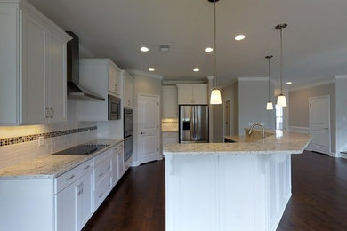 Example of a large transitional l-shaped medium tone wood floor eat-in kitchen design in Atlanta with an undermount sink, white backsplash, ceramic backsplash, stainless steel appliances, an island, granite countertops, shaker cabinets and white cabinets