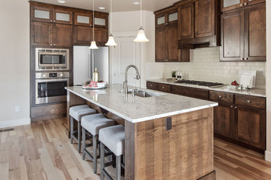 Inspiration for a mid-sized transitional l-shaped light wood floor open concept kitchen remodel in Boise with an undermount sink, raised-panel cabinets, medium tone wood cabinets, granite countertops, white backsplash, subway tile backsplash, stainless steel appliances and an island