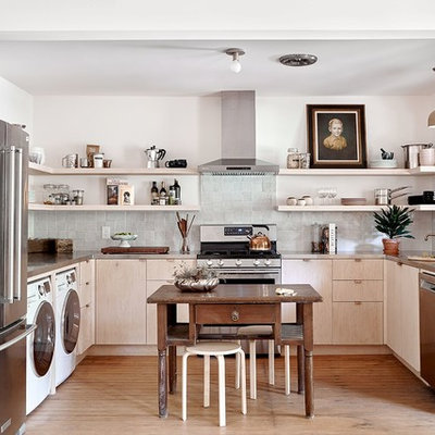 Example of a trendy u-shaped medium tone wood floor and brown floor kitchen design in Austin with an undermount sink, flat-panel cabinets, light wood cabinets, gray backsplash, mosaic tile backsplash, stainless steel appliances and an island