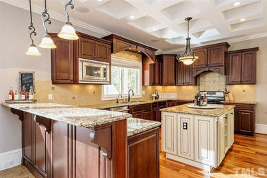 Inspiration for a mid-sized timeless u-shaped medium tone wood floor and brown floor kitchen remodel in Raleigh with an undermount sink, raised-panel cabinets, dark wood cabinets, granite countertops, beige backsplash, terra-cotta backsplash, stainless steel appliances, an island and multicolored countertops