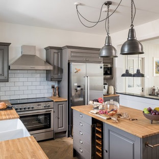Inspiration for a nautical l-shaped kitchen/diner in Cornwall with a double-bowl sink, raised-panel cabinets, grey cabinets, wood worktops, white splashback, metro tiled splashback, stainless steel appliances, medium hardwood flooring, an island, brown floors and brown worktops.