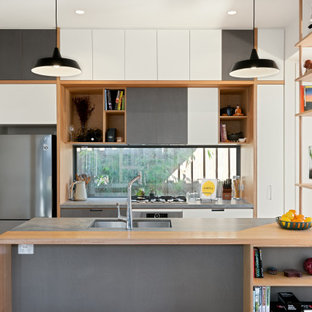 Mid-sized contemporary galley open plan kitchen in Melbourne with an undermount sink, flat-panel cabinets, window splashback, stainless steel appliances, with island, grey benchtop, white cabinets, medium hardwood floors and brown floor.