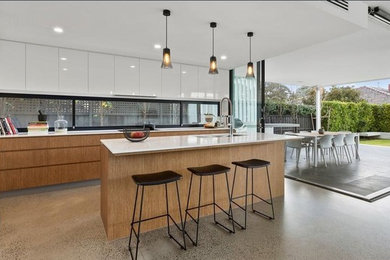 Photo of a contemporary galley open plan kitchen in Melbourne with flat-panel cabinets, medium wood cabinets, window splashback, concrete flooring, an island, grey floors and white worktops.