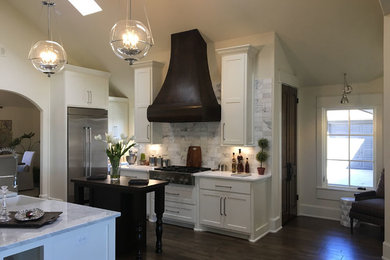 Large transitional l-shaped dark wood floor and brown floor open concept kitchen photo in Austin with a farmhouse sink, recessed-panel cabinets, white cabinets, marble countertops, white backsplash, marble backsplash, stainless steel appliances, two islands and white countertops